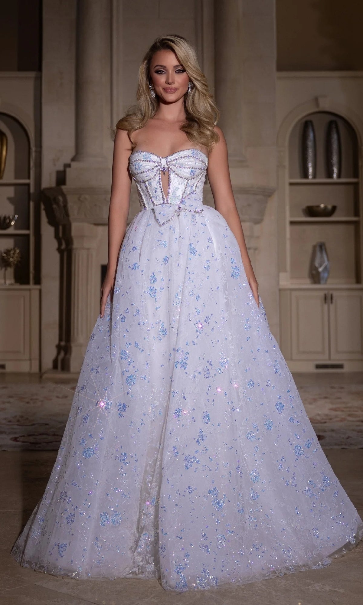A woman wearing the Portia and Scarlett PS25315 long prom dress with blue sparkly floral details and a sweetheart neckline stands indoors against an elegant, classical background.